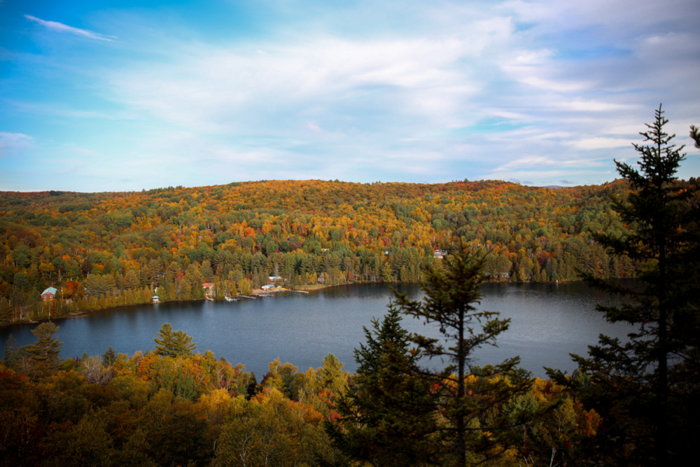Vue panoramique d’un lac bordé de chalets et de forêts aux couleurs automnales, près des hébergements de Chalets Lanaudière.