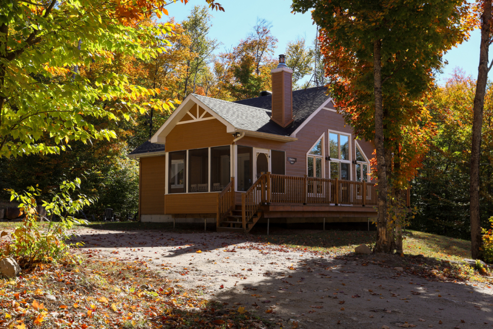 Chalet de Chalets Lanaudière entouré d’arbres colorés à l’automne, avec terrasse couverte et grandes fenêtres.