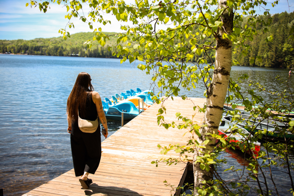 Personne marchant sur un quai au bord d’un lac, près de pédalos, dans un décor forestier de Chalets Lanaudière.