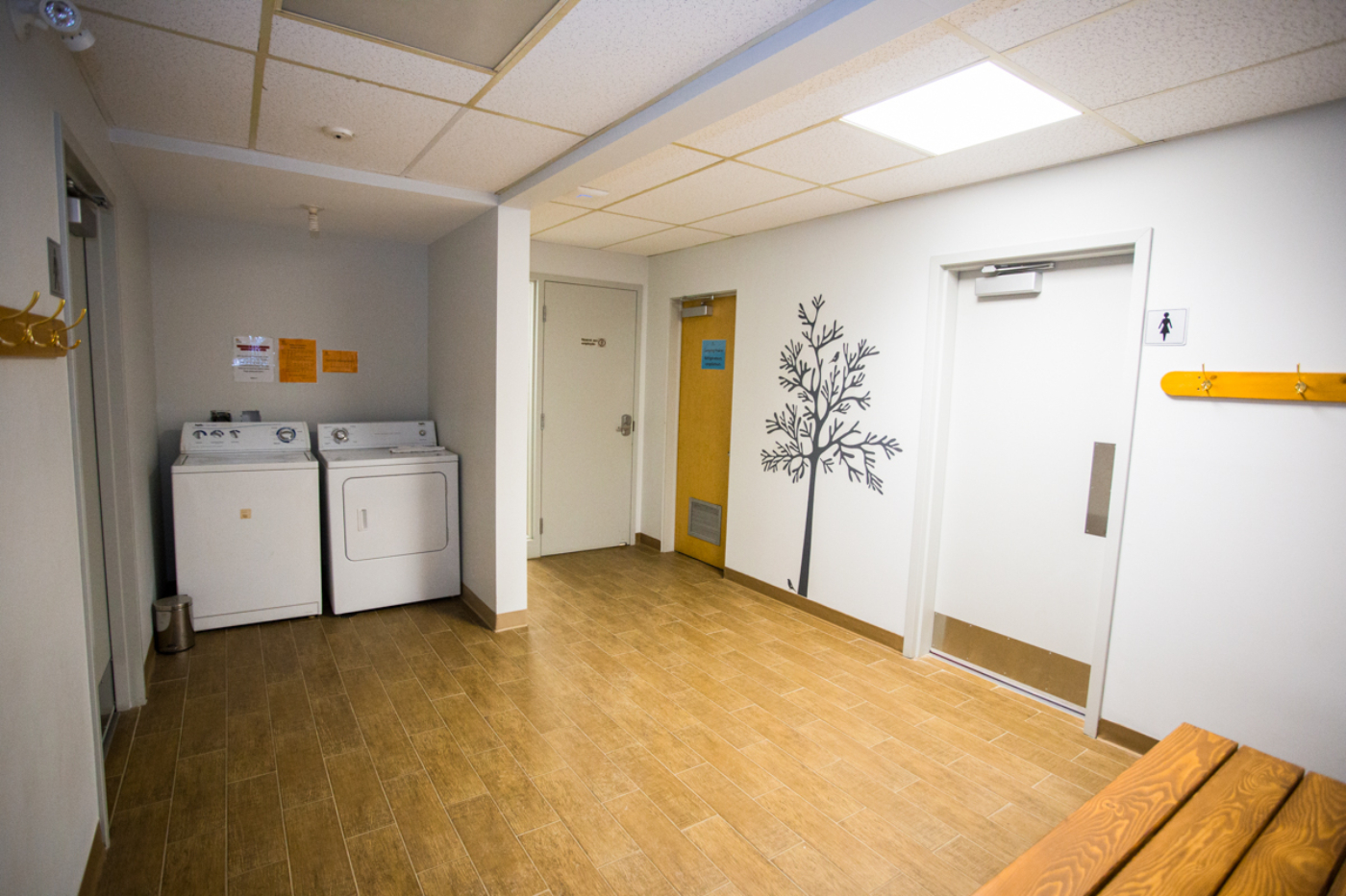 Buanderie commune avec laveuses, sécheuses, portes d’accès et banc en bois dans un chalet de Chalets Lanaudière