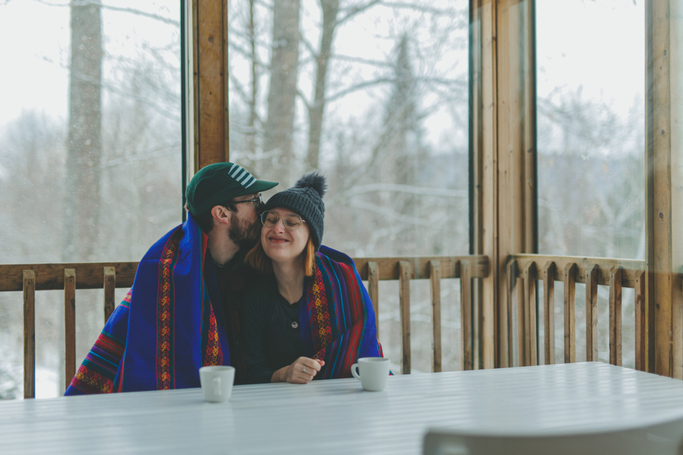 Couple profitant d’un moment chaleureux sur la véranda vitrée d’un chalet de Chalets Lanaudière, avec vue sur la forêt enneigée.