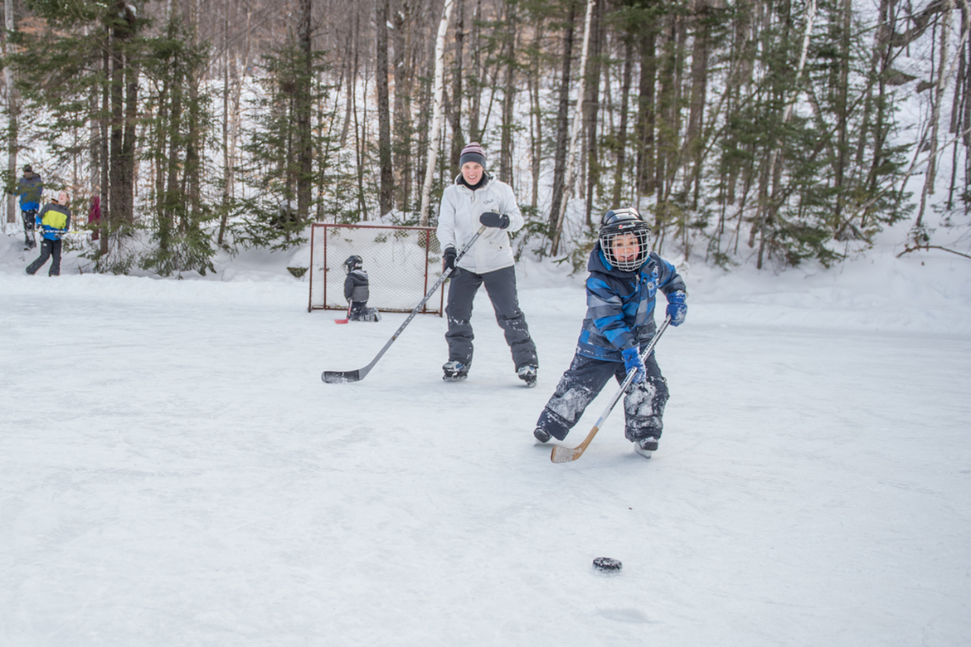 Enfants et adulte jouent au hockey sur une patinoire extérieure enneigée de Chalets Lanaudière.