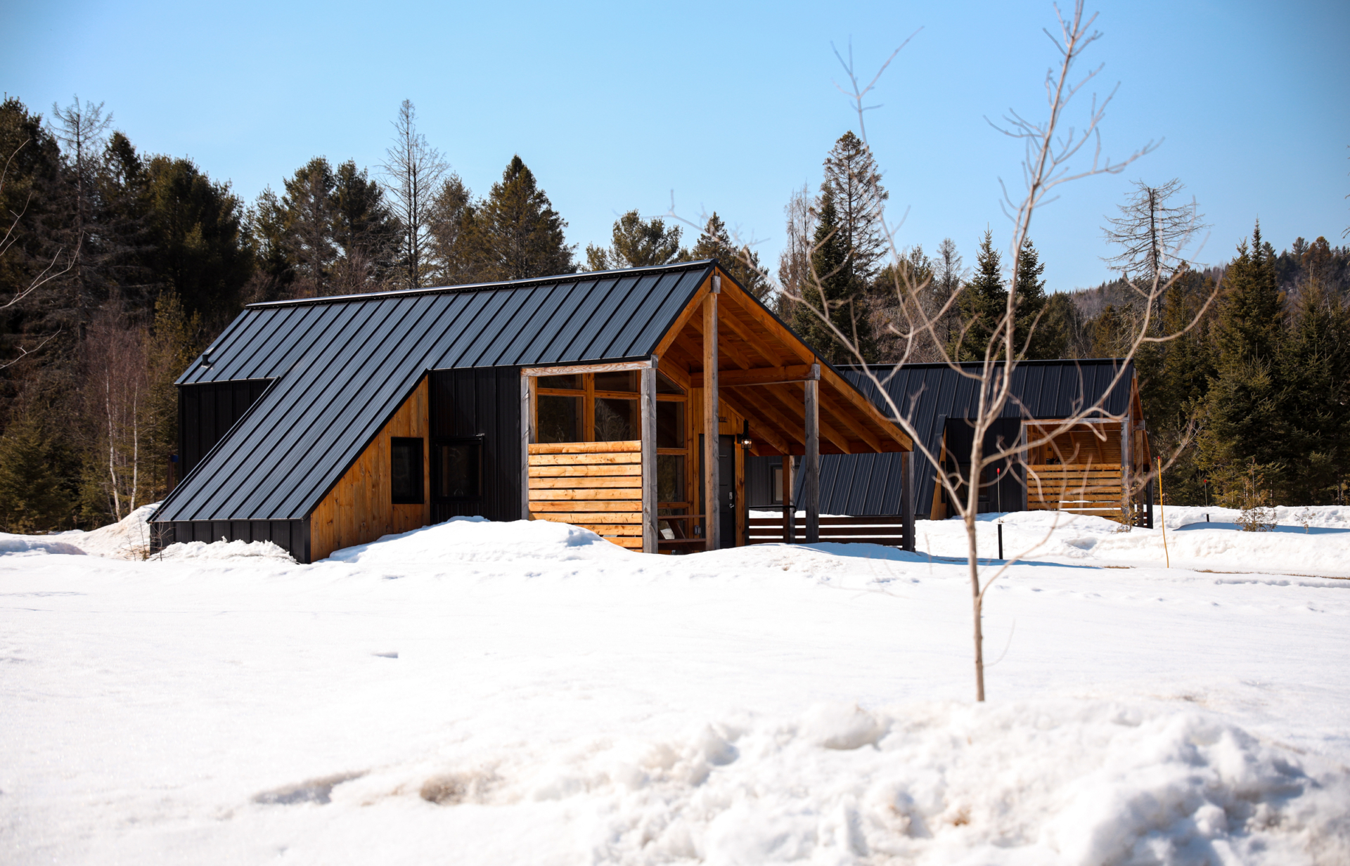 Chalet en bois de Chalets Lanaudière, entouré de neige et de forêt, avec grande terrasse couverte.