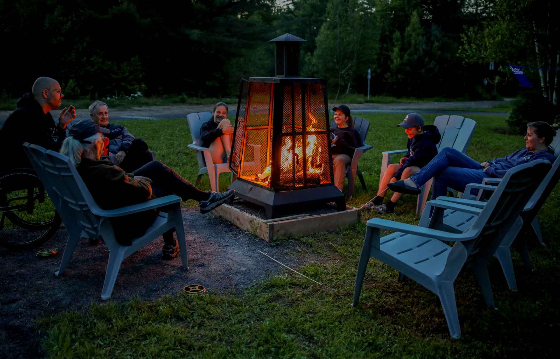Groupe profitant d’un feu extérieur en soirée au camping de Chalets Lanaudière, assis dans des fauteuils Adirondack.