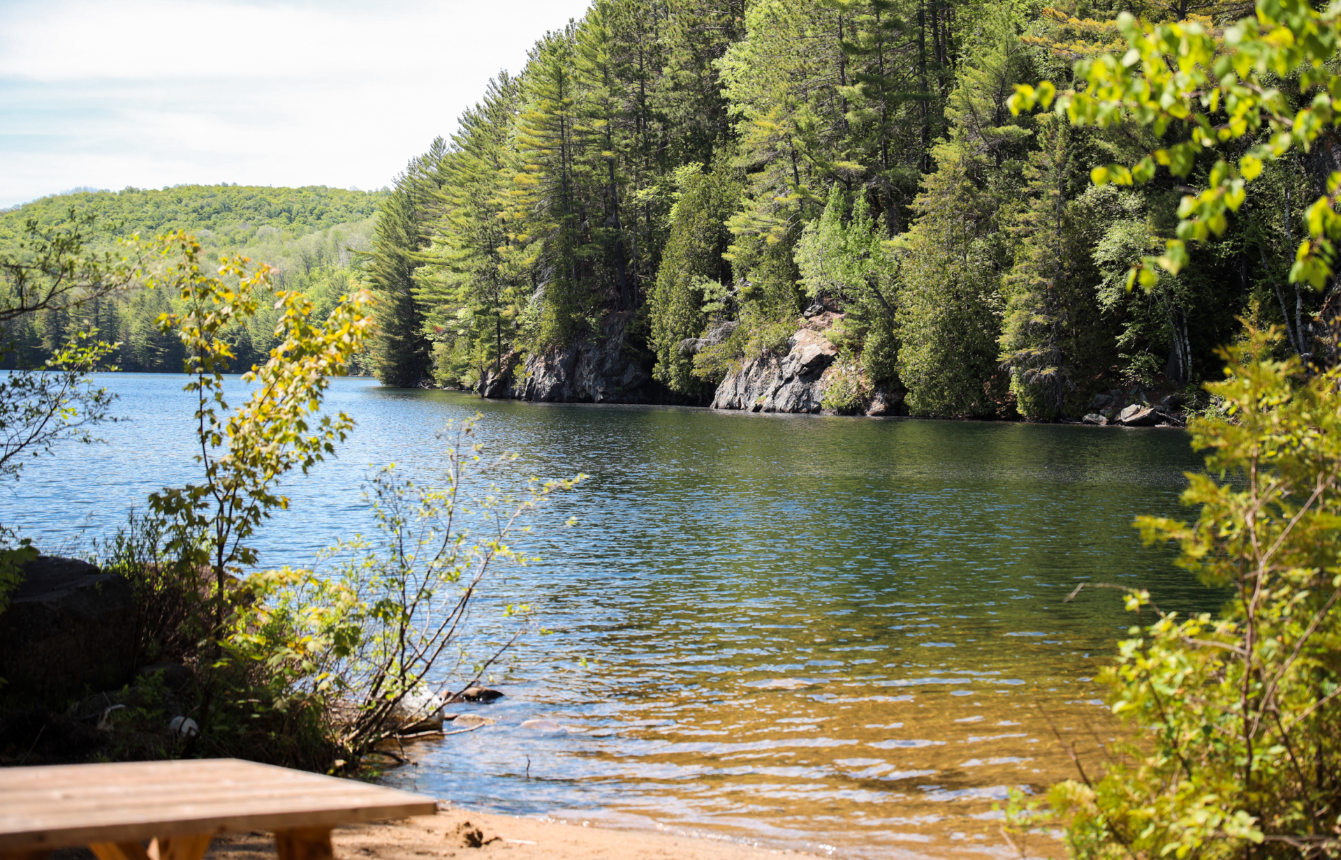 Lac paisible bordé d’une forêt dense, vu depuis la rive d’un site de camping des Chalets Lanaudière.