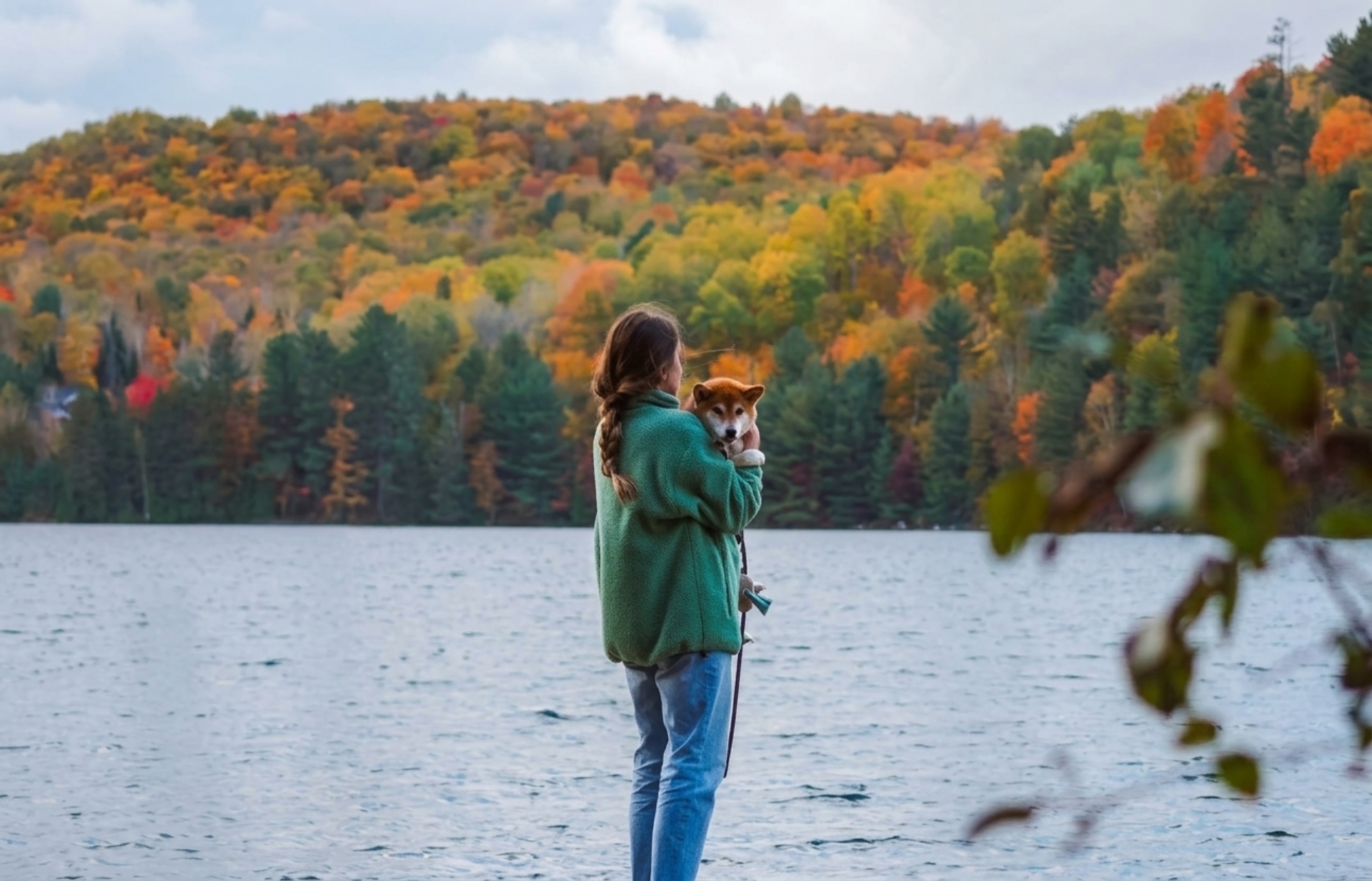 Personne tenant un chien au bord d’un lac, entourée des couleurs automnales de la nature près des chalets Lanaudière.