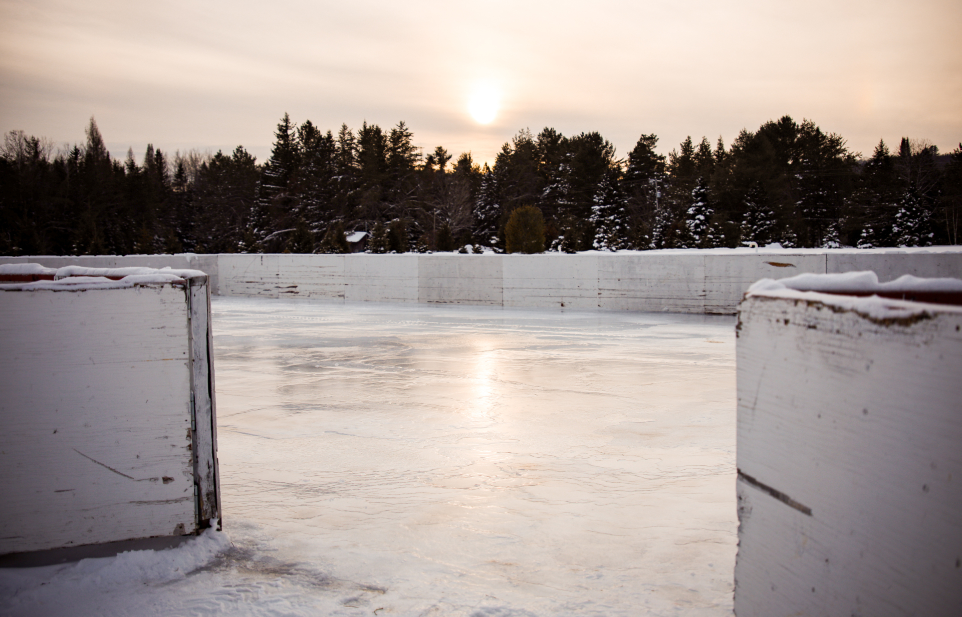 Patinoire extérieure enneigée dans un environnement boisé, avec le soleil couchant en arrière-plan, près des chalets Lanaudière.