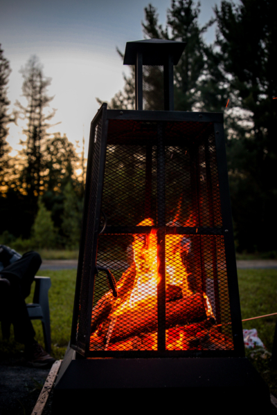 Foyer extérieur dans une cheminée grillagée, au coucher du soleil, sur un terrain de camping de Chalets Lanaudière.