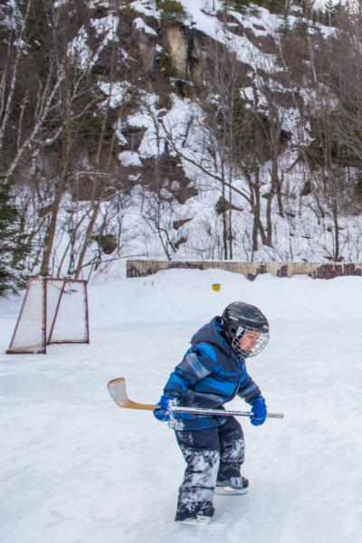 Enfant jouant au hockey sur une patinoire enneigée près des chalets Lanaudière, avec un filet et une forêt en arrière-plan.