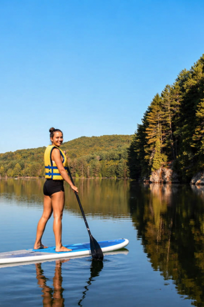 Personne faisant du paddleboard sur un lac paisible entouré de forêts, près des chalets de Chalets Lanaudière.