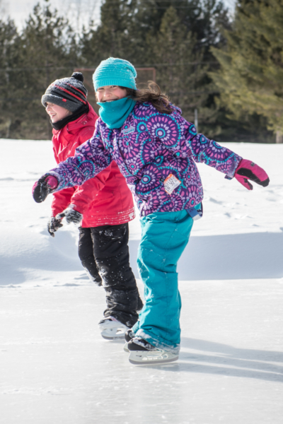Deux enfants s’amusent à patiner sur la glace enneigée lors de leur séjour aux Chalets Lanaudière.