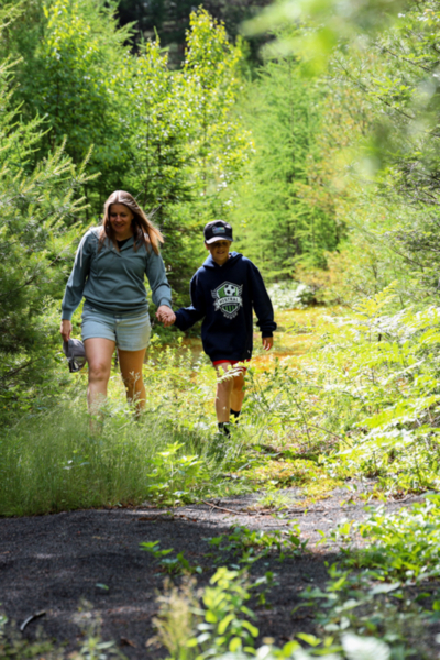 Mère et enfant marchant main dans la main sur un sentier forestier près d’un chalet de Chalets Lanaudière.