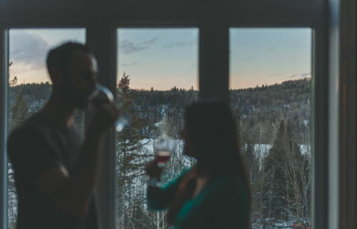 Personnes profitant d’un moment convivial dans un chalet de Chalets Lanaudière, avec vue sur une forêt enneigée au coucher du soleil.