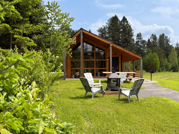 Chalet en bois de Chalets Lanaudière avec terrasse couverte, foyer extérieur et fauteuils, entouré de verdure.