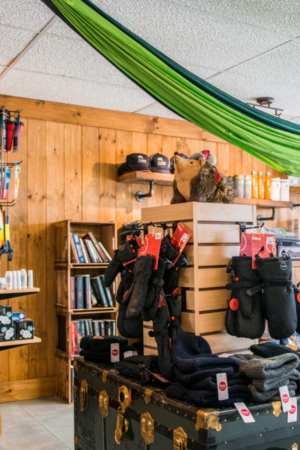 Boutique de Chalets Lanaudière avec hamacs, vêtements chauds, livres et équipement de plein air présentés dans un décor boisé.