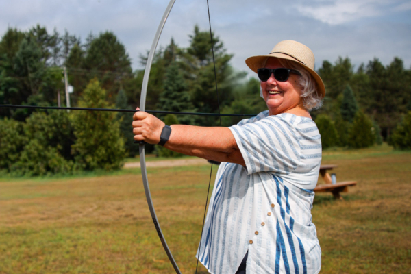 Personne souriante pratiquant le tir à l’arc en plein air sur le terrain d’un camping Chalets Lanaudière.