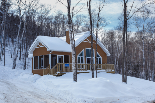 Chalet chaleureux de Chalets Lanaudière niché dans une forêt enneigée, avec terrasse et grandes fenêtres donnant sur l’hiver.