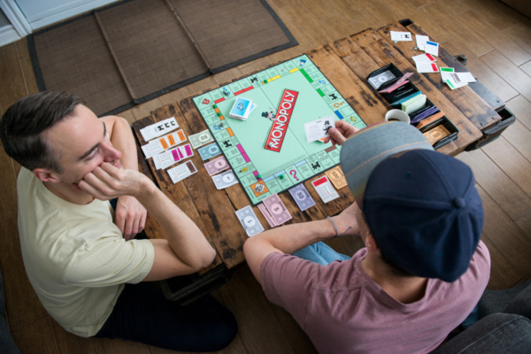 Deux personnes jouent au Monopoly autour d’une table en bois dans un chalet de Chalets Lanaudière.