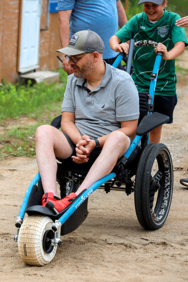 Personne en fauteuil roulant tout-terrain, poussée par un accompagnateur lors d’une activité de plein air à Chalets Lanaudière.