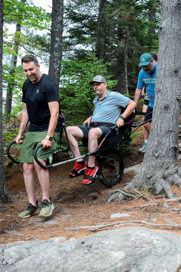 Groupe en randonnée dans la forêt, transportant une personne en fauteuil tout-terrain près des chalets de Chalets Lanaudière.