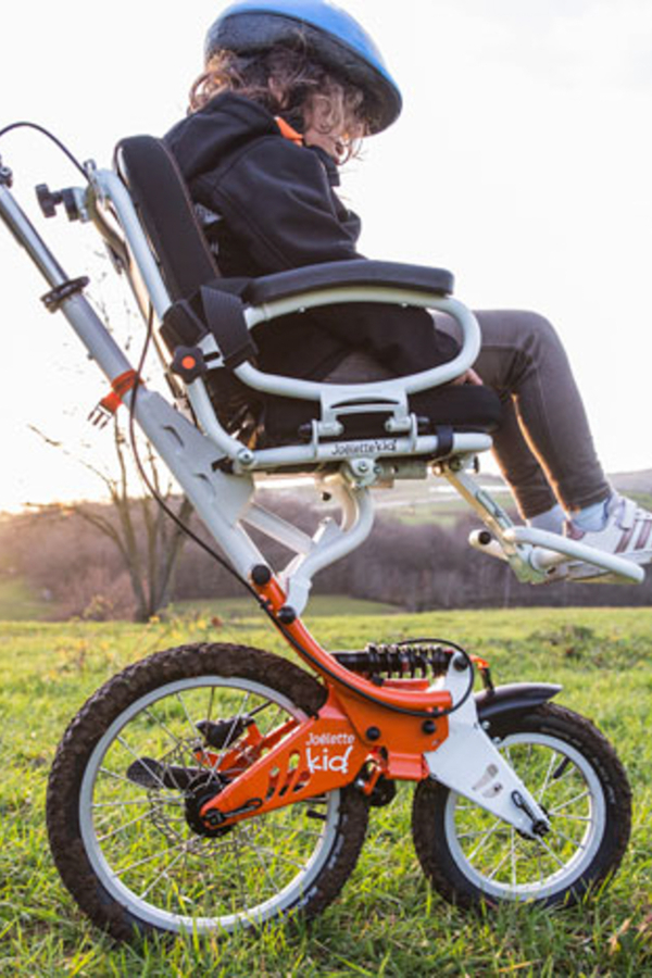 Enfant profitant d’une promenade en plein air dans un fauteuil roulant tout-terrain, au coucher du soleil.