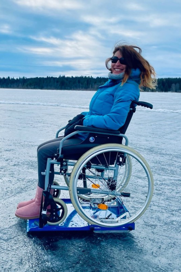 Personne souriante en fauteuil roulant sur un lac gelé, profitant de l’hiver près des chalets de Chalets Lanaudière.