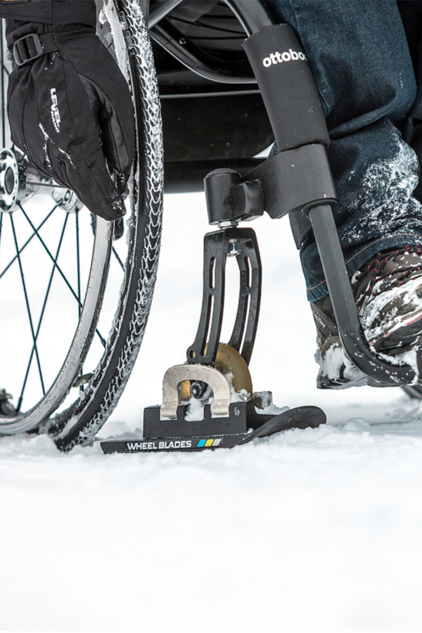 Skieur utilisant un appareil de ski adapté à une roue de fauteuil roulant sur un sentier enneigé.