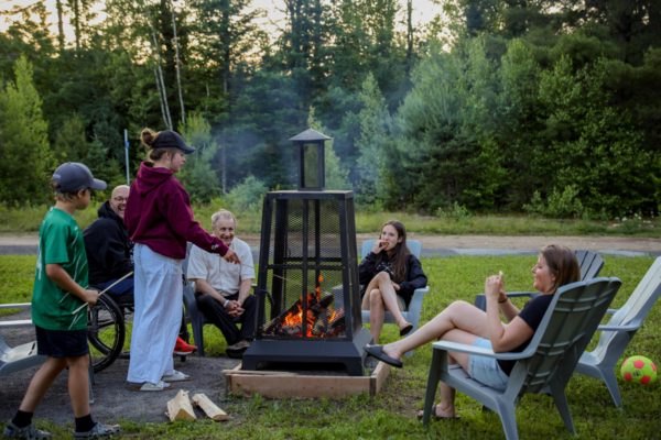 Groupe profitant d’un feu extérieur dans un camping de Chalets Lanaudière, avec des chaises Adirondack et un terrain boisé.