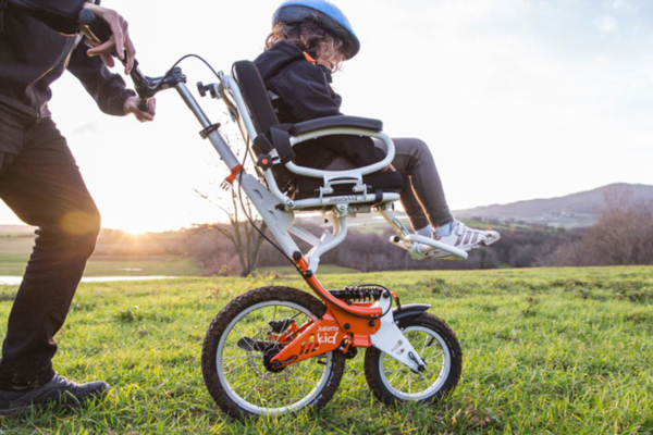 Personne utilisant une poussette tout-terrain adaptée dans un champ, accompagnée d’une autre personne, au coucher du soleil.