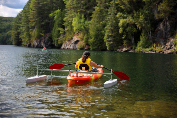 Person pagayant en kayak sur un lac bordé de forêt et de falaises, lors d’un séjour de plein air aux Chalets Lanaudière.