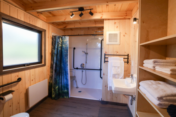 Salle de bain en bois d’un chalet de Chalets Lanaudière, avec douche accessible, lavabo et serviettes pliées.