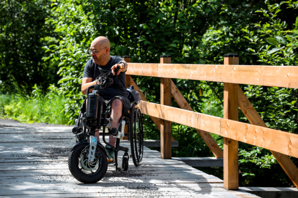 Personne en fauteuil roulant profitant d’une promenade en forêt sur une passerelle accessible près d’un chalet de Chalets Lanaudière.