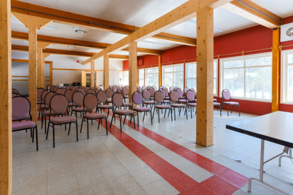 Grande salle de réunion lumineuse avec nombreuses chaises, poutres en bois et fenêtres, dans un établissement de Chalets Lanaudière.