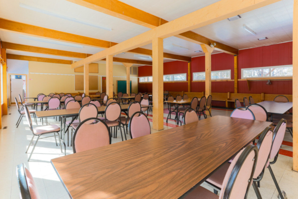 Grande salle commune de Chalets Lanaudière avec tables en bois et nombreuses chaises, idéale pour les repas et rassemblements.
