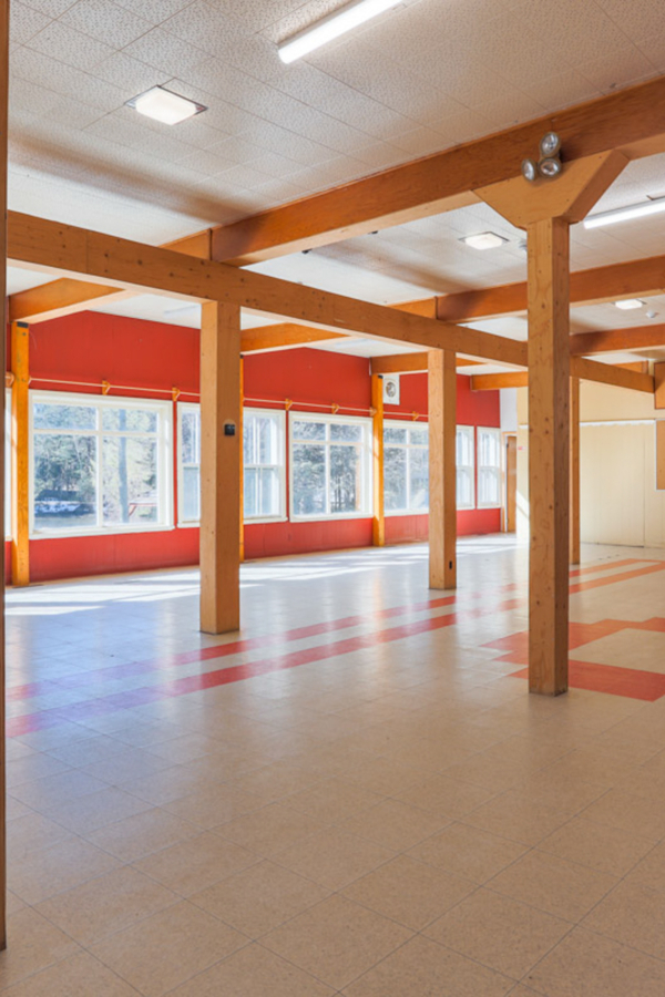 Salle intérieure spacieuse d’un chalet de Chalets Lanaudière, avec poutres en bois, grandes fenêtres et plancher coloré.