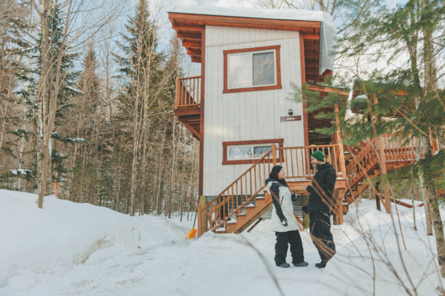 Deux personnes en hiver devant un petit chalet en bois enneigé de Chalets Lanaudière.