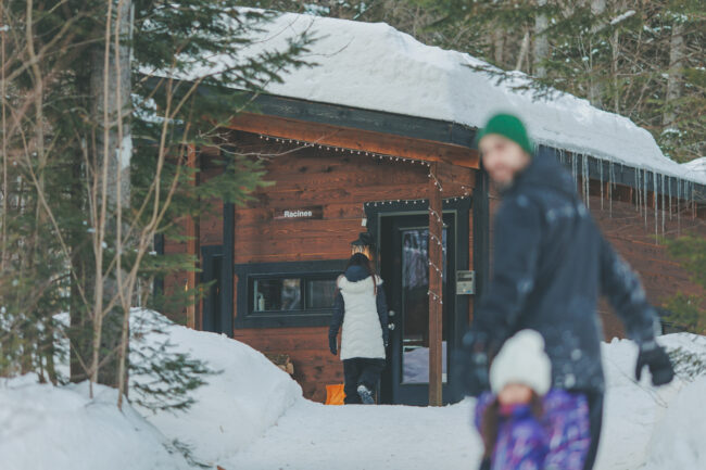 Personnes profitant d’un chalet enneigé de Chalets Lanaudière, avec sapins et glaçons en hiver.