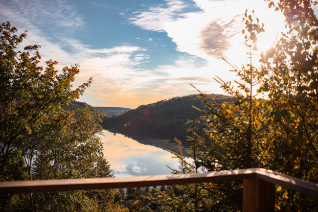 Vue panoramique d’un lac entouré de collines boisées depuis la terrasse d’un chalet de Chalets Lanaudière, au coucher du soleil.