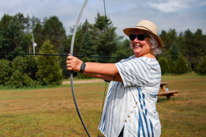 Personne souriante pratiquant le tir à l’arc en plein air sur le terrain d’un camping Chalets Lanaudière.