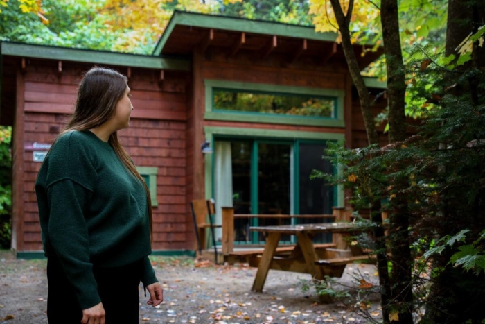 Personne admirant l’extérieur d’un chalet en bois de Chalets Lanaudière, entouré d’arbres aux couleurs automnales.