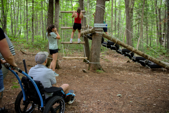 Personnes profitant d’un parcours d’aventure en forêt chez Chalets Lanaudière, avec une personne en fauteuil roulant au premier plan.