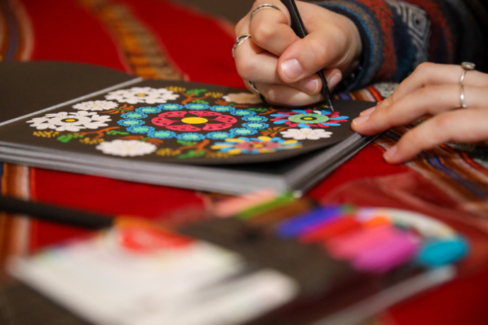 Personne coloriant un motif floral complexe dans un cahier, avec des crayons de couleur, lors d’une activité en chalet.