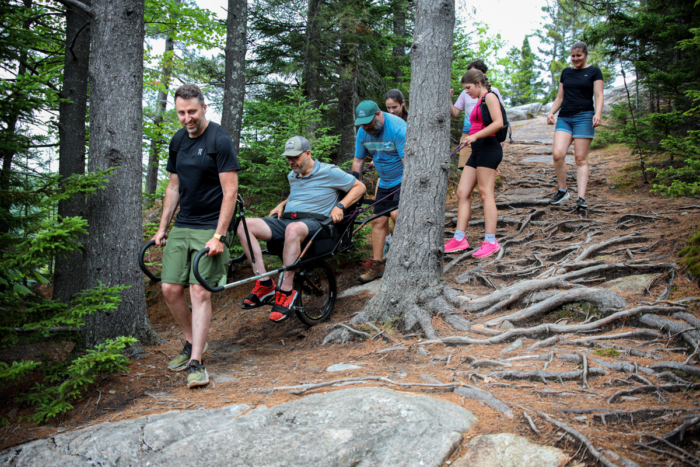 Groupe profitant d’une randonnée en forêt près des chalets de Chalets Lanaudière, avec une personne aidée en fauteuil tout-terrain.