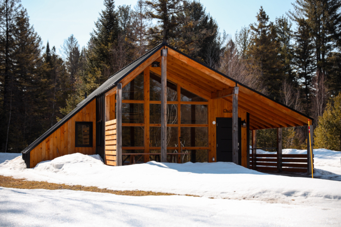 Chalet en bois de Chalets Lanaudière entouré d’arbres enneigés, avec grande façade vitrée et toit en pente.