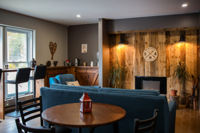 Salon chaleureux d’un chalet de Chalets Lanaudière avec foyer, canapé bleu, bar, table à manger et décor rustique en bois.