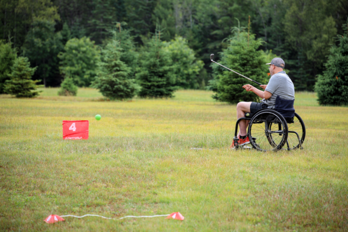 Personne en fauteuil roulant jouant au golf sur le terrain gazonné d’un établissement de Chalets Lanaudière.
