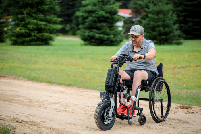 Personne en fauteuil roulant adapté roulant sur un sentier de terre dans un environnement naturel près des chalets Lanaudière.