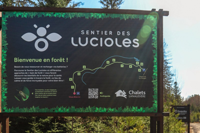 Panneau d’accueil du sentier des Lucioles en forêt, avec carte du parcours et logo de Chalets Lanaudière.