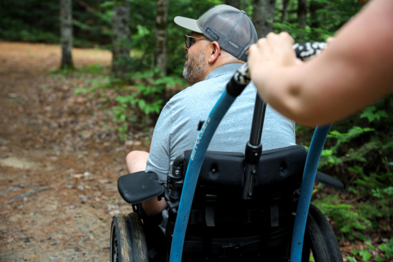 Personne en fauteuil roulant poussée sur un sentier forestier près d’un hébergement de Chalets Lanaudière.