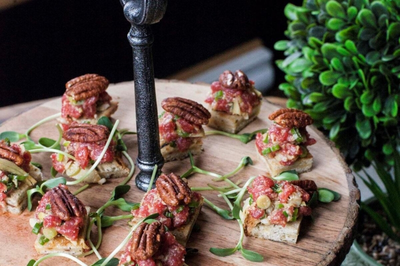 Bouchées gourmandes garnies de viande, légumes et pacanes, présentées sur une planche de bois.